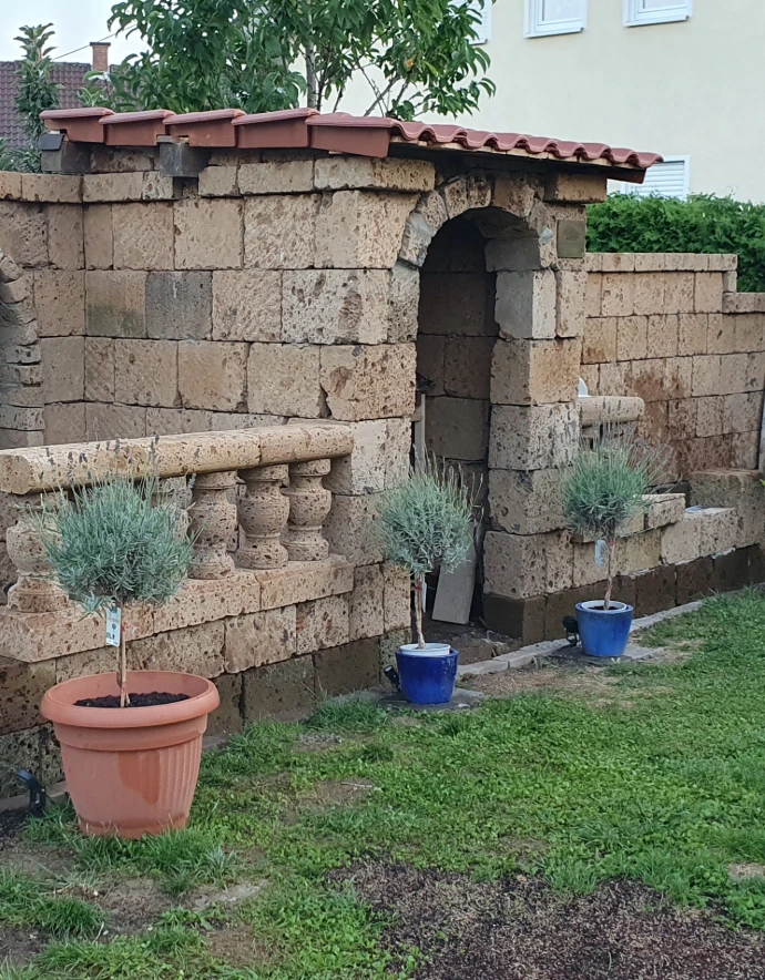 Pflanzgefäße vor einer Tuffmauer im Garten