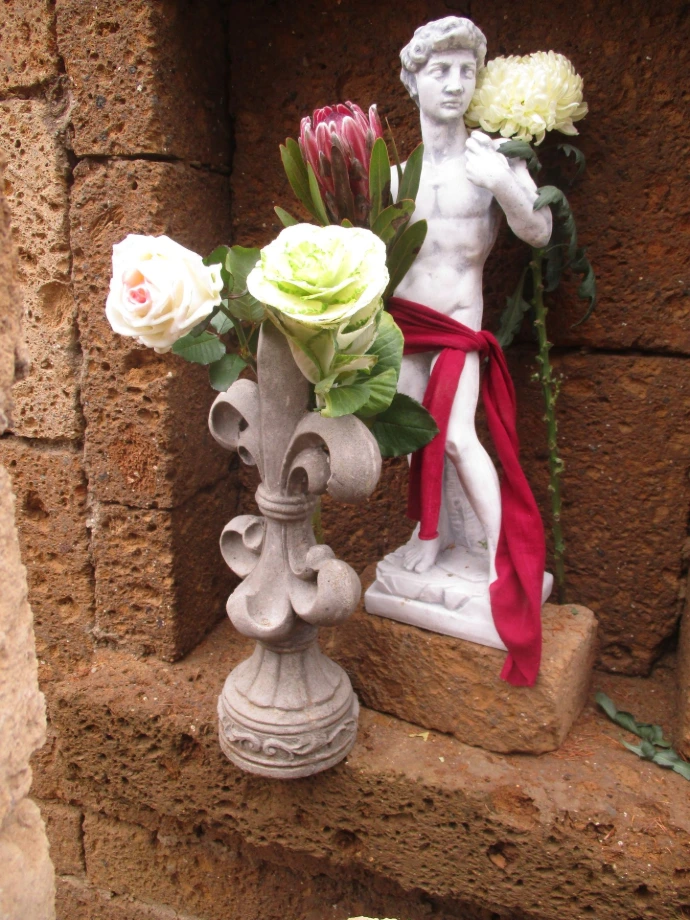 Kleine Dekoration mit Figur und Blüten in einer Mauernische